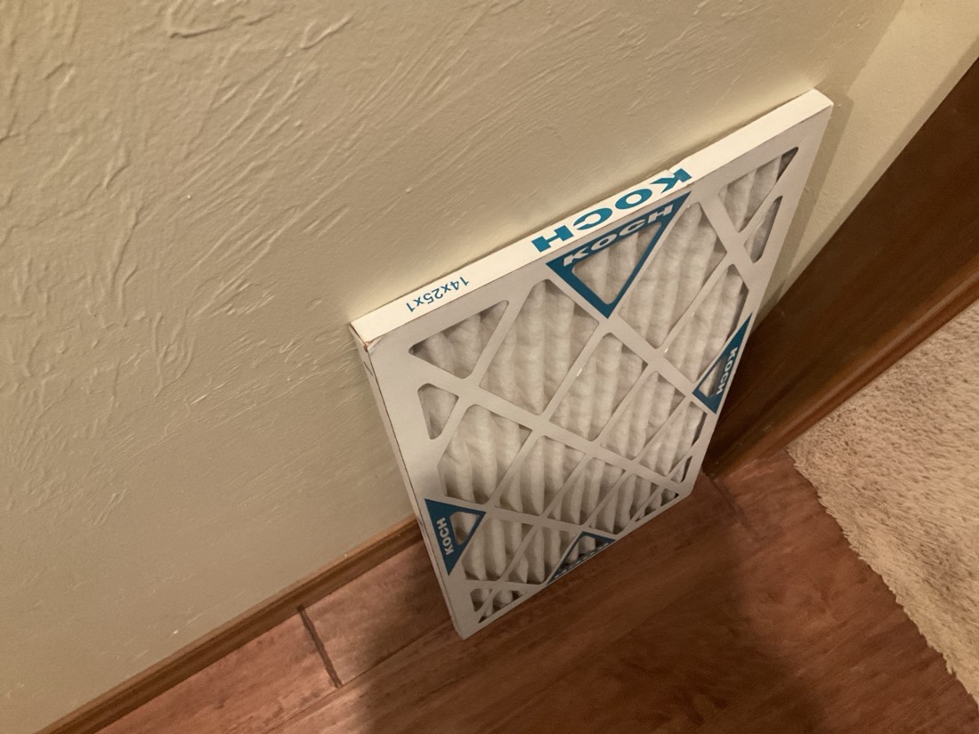 White pleated air filter with blue frame installed in return air duct system.