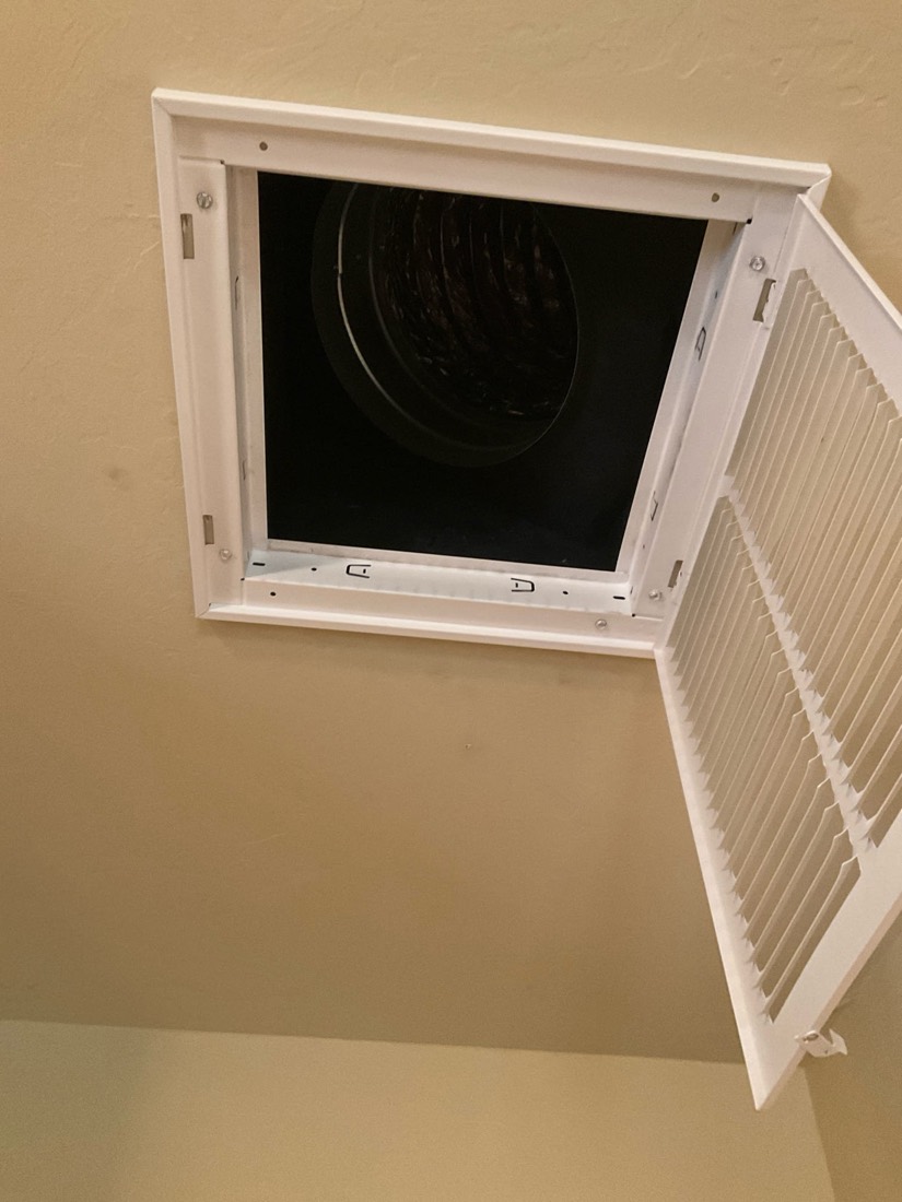 White return air duct access cover mounted on wall with dark ductwork interior visible.