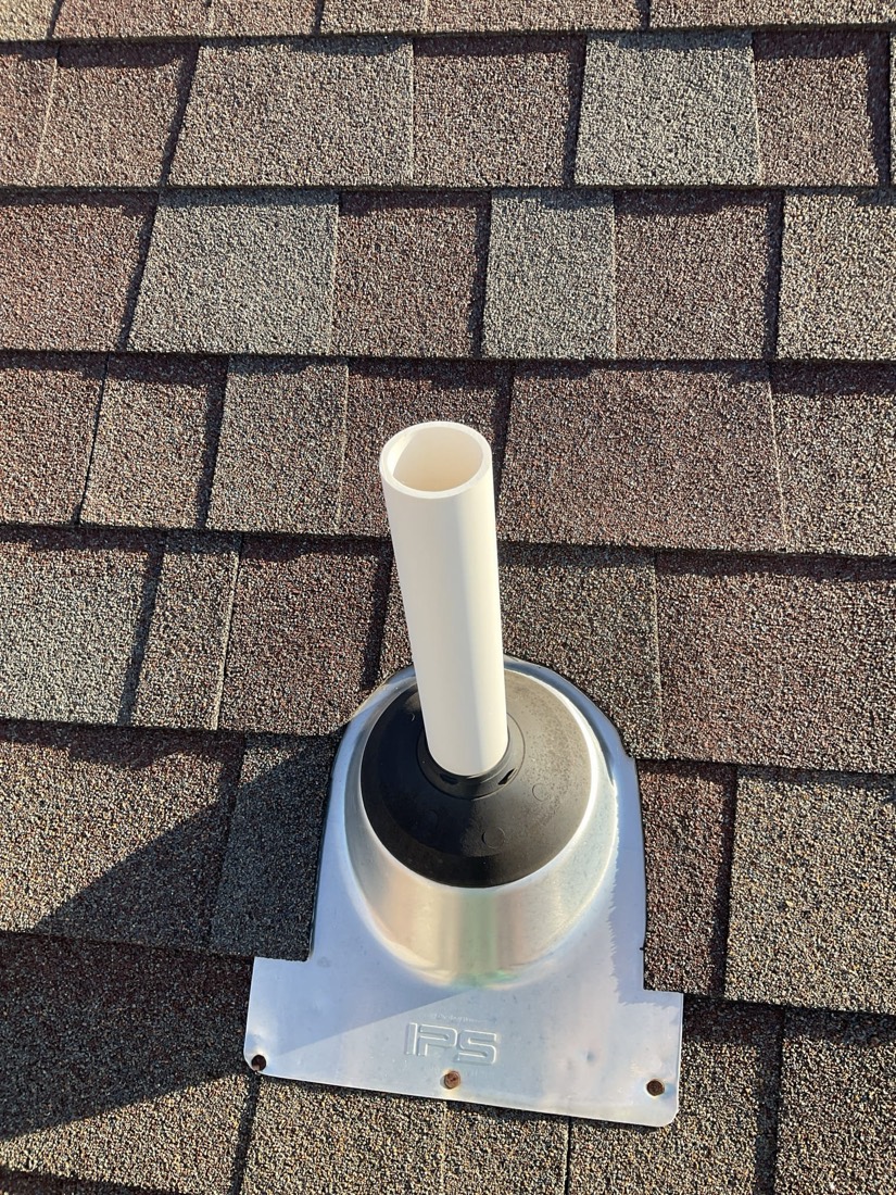 White PVC pipe flashing mounted on asphalt shingle roof.