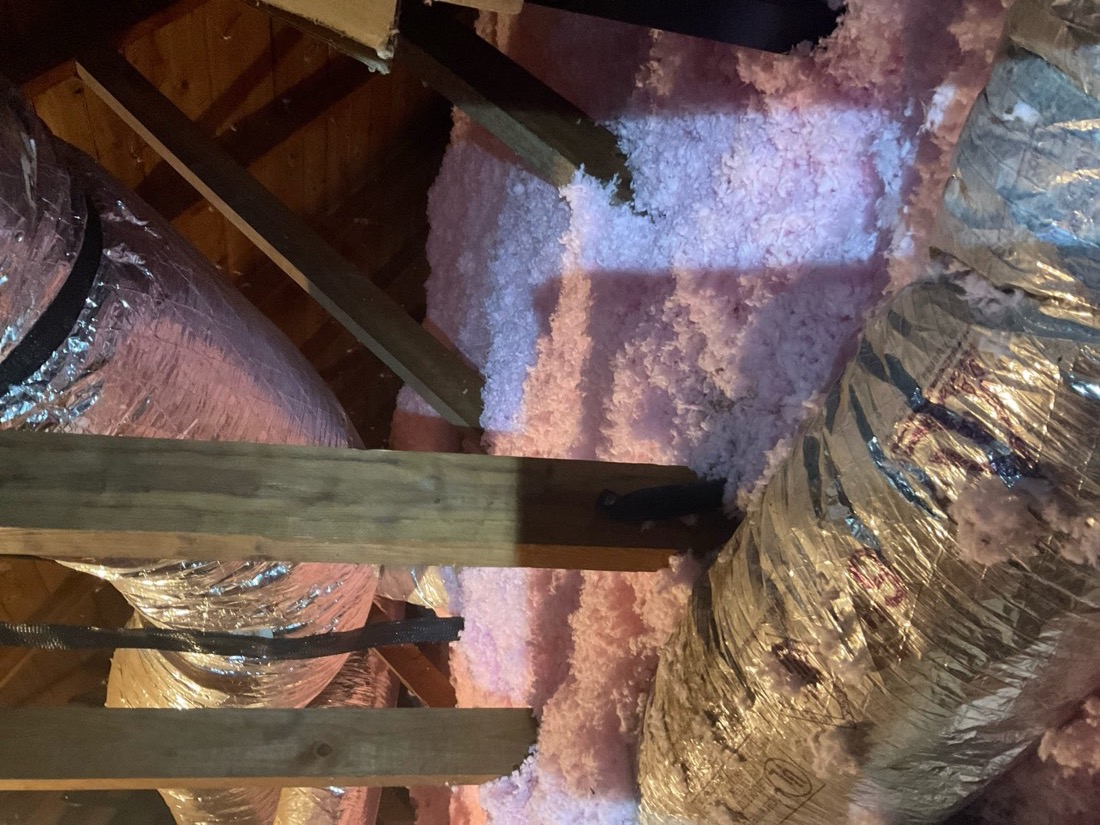 New fiberglass insulation batts and ductwork in attic installation.
