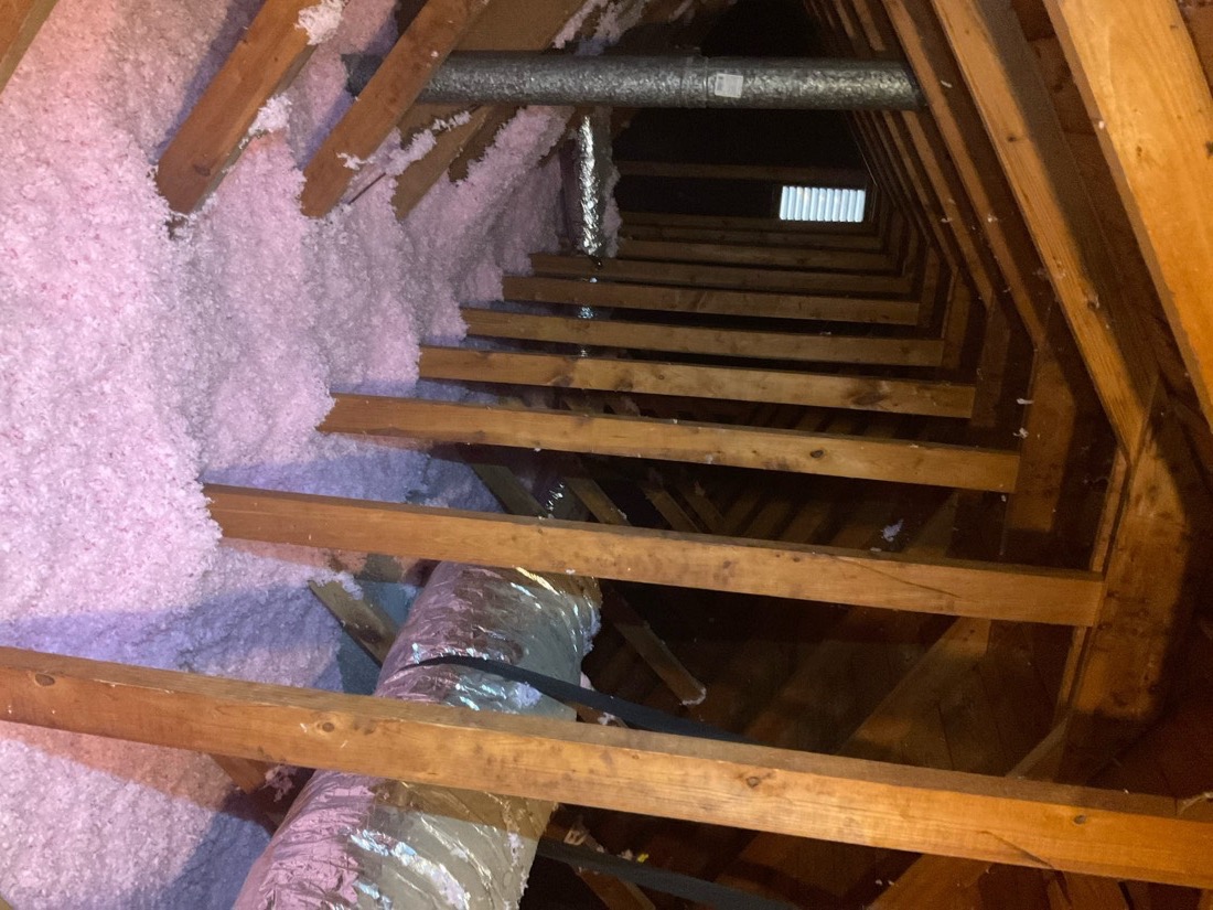 Properly installed fiberglass insulation batts in attic space with wooden framing.