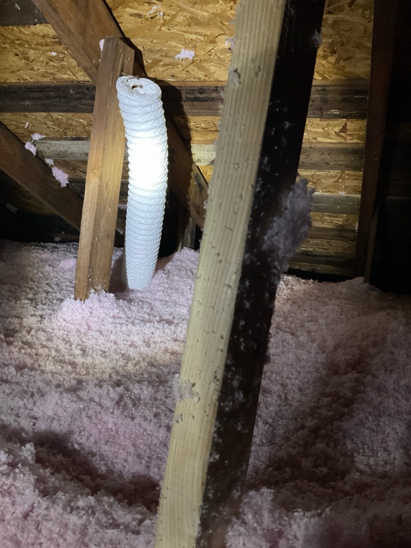 Wrapped ventilation duct surrounded by blown-in pink insulation in attic.