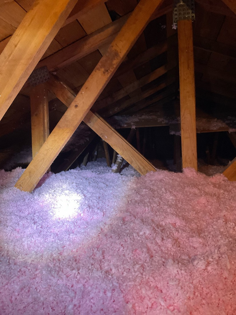 Blown-in attic insulation installed between wooden rafters in attic space