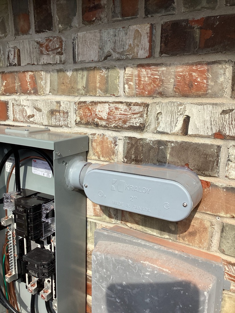 Gray outlet cover and conduit installed on brick exterior foundation.