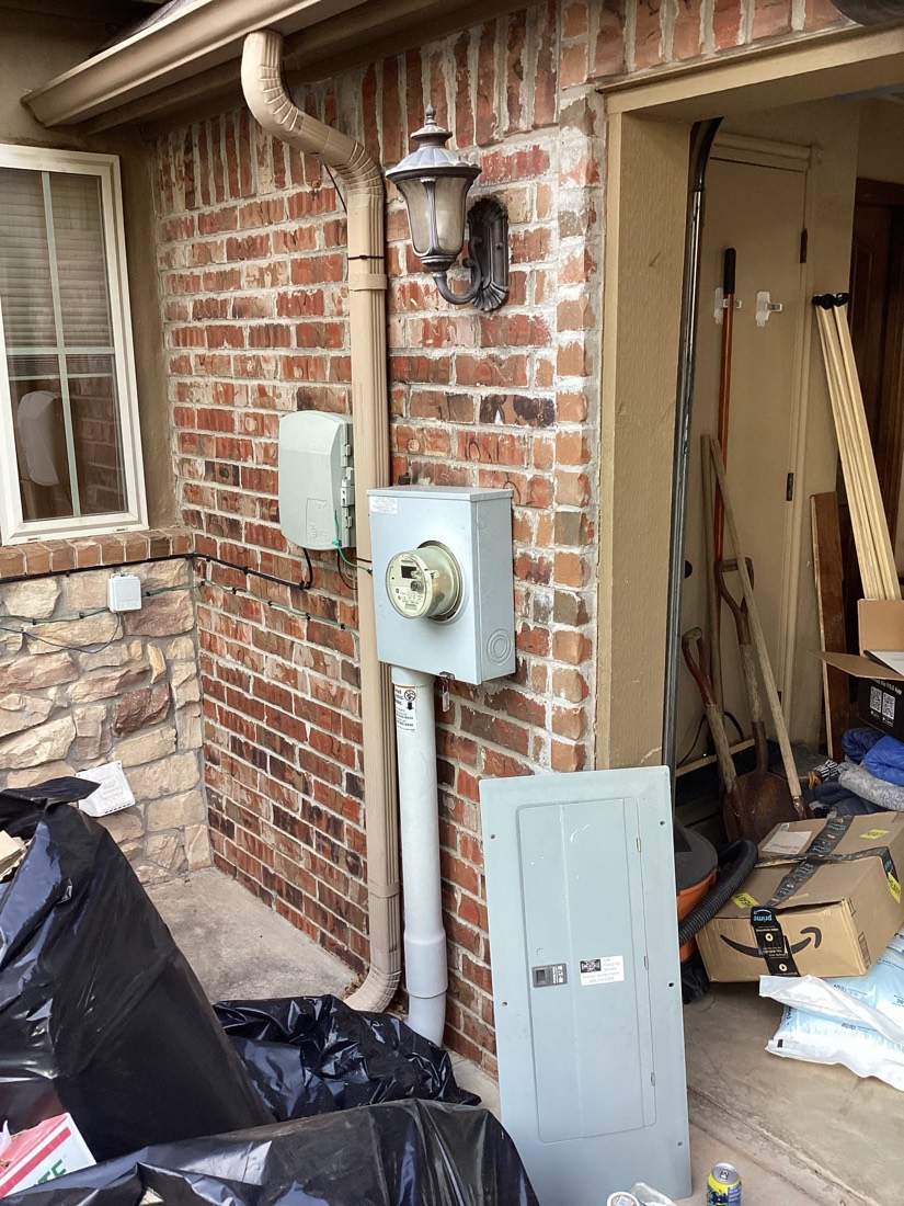 White electrical meter mounted on red brick wall with conduit.
