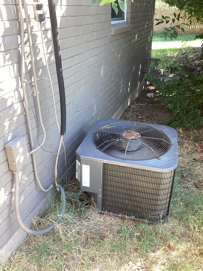 Outdoor air conditioning condenser unit with blue fan cover mounted against brick wall