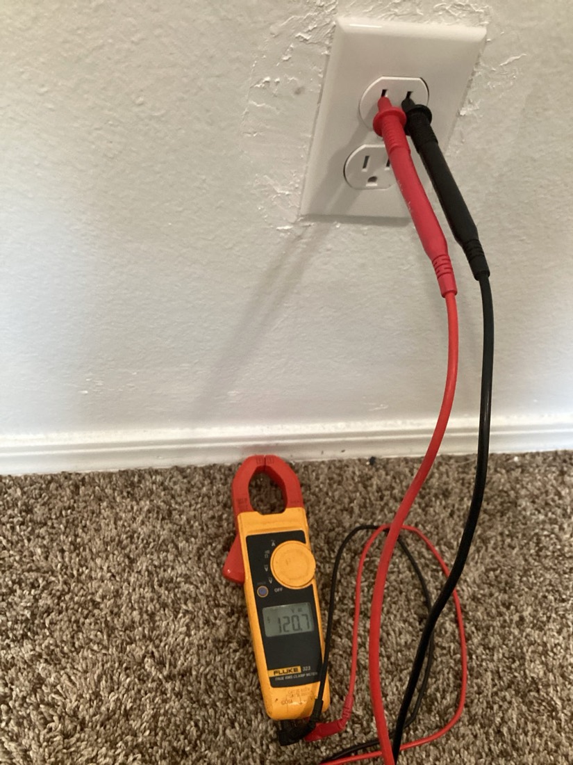 Clamp meter connected to outlet leads for electrical testing.