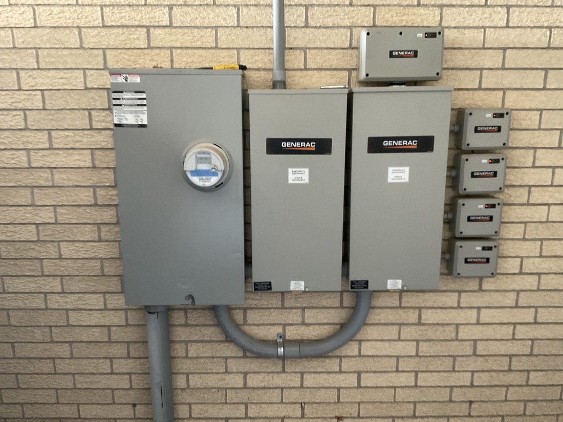 Generac generators with meter and electrical disconnect switches on brick wall.
