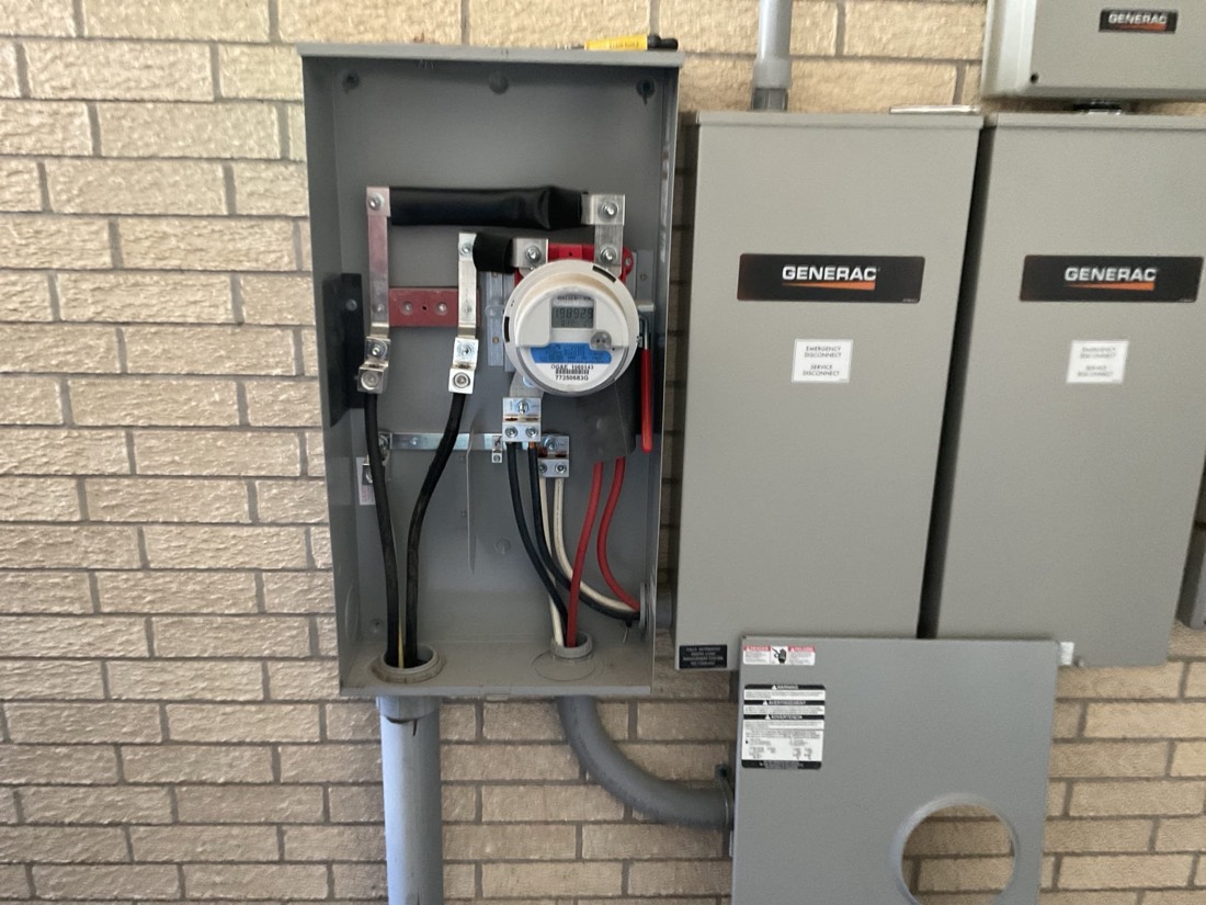 Generac generator units with meter and electrical disconnect panel mounted on brick.