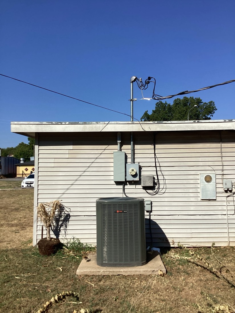 Outdoor AC unit mounted on concrete pad with condenser lines and electrical connections visible.