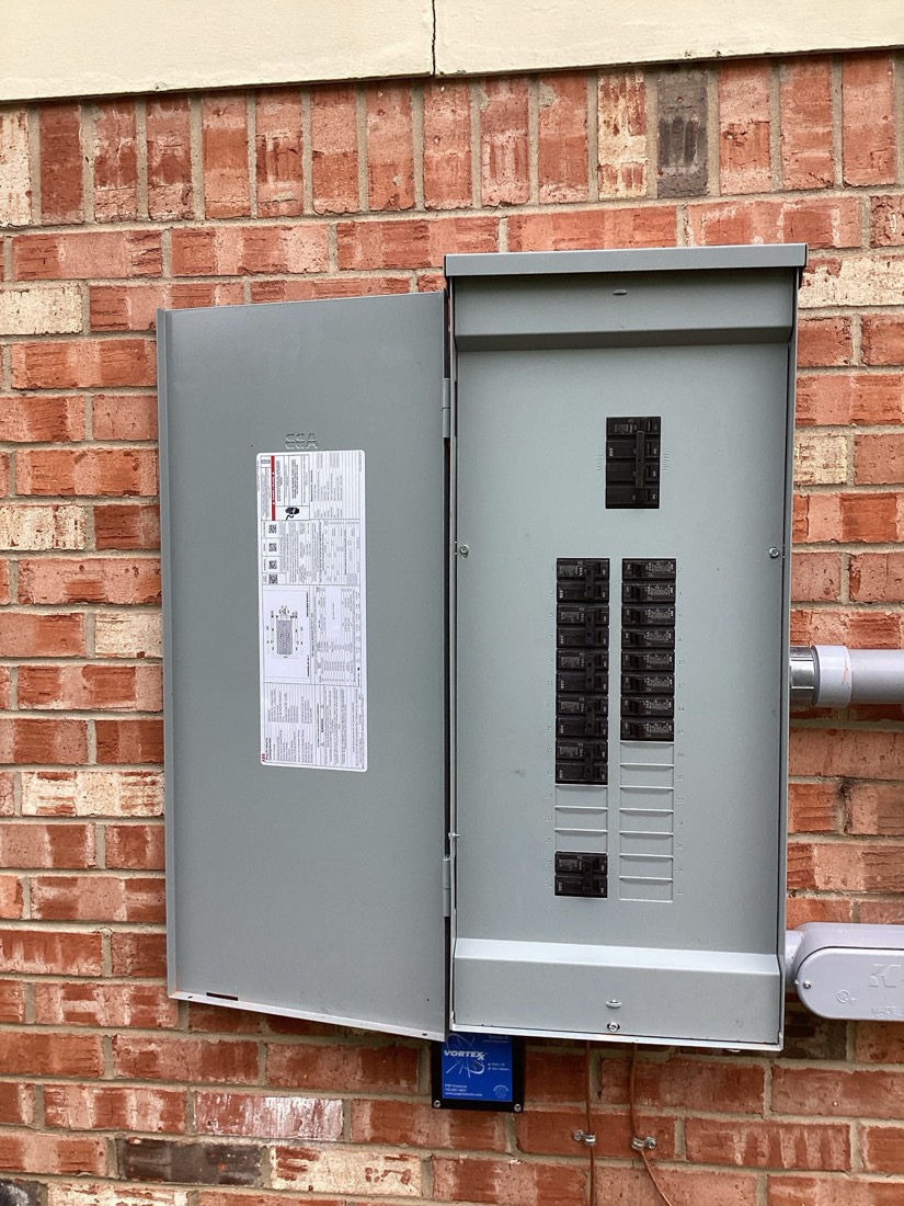 New gray main electrical panel with circuit breakers on brick exterior.