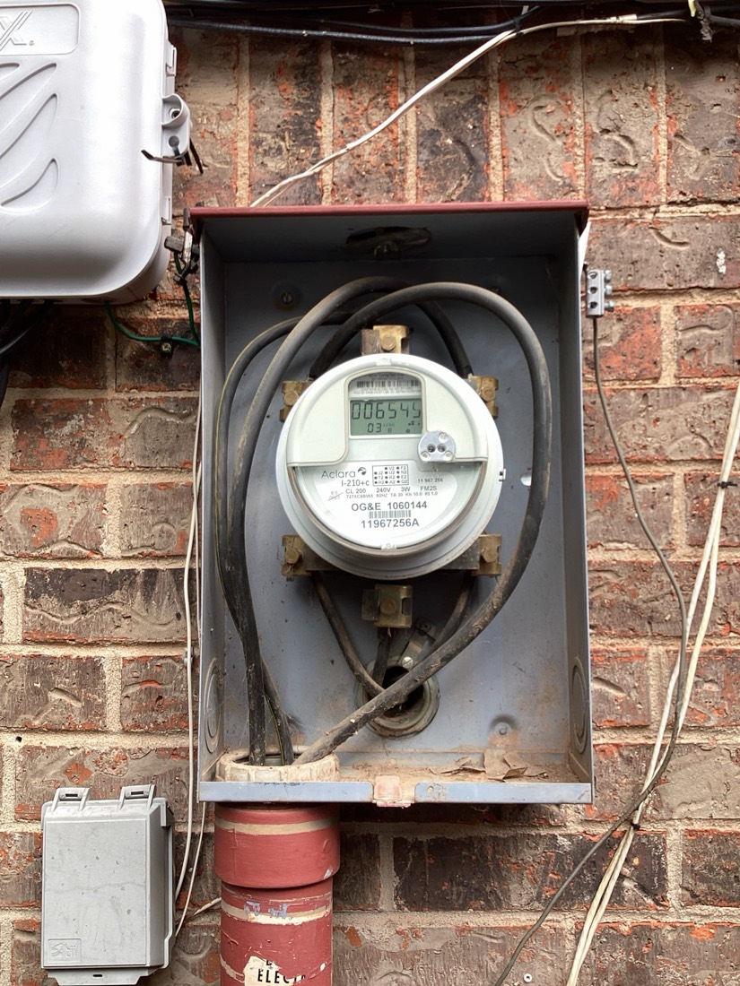Electric meter mounted on brick exterior wall with service lines connected.