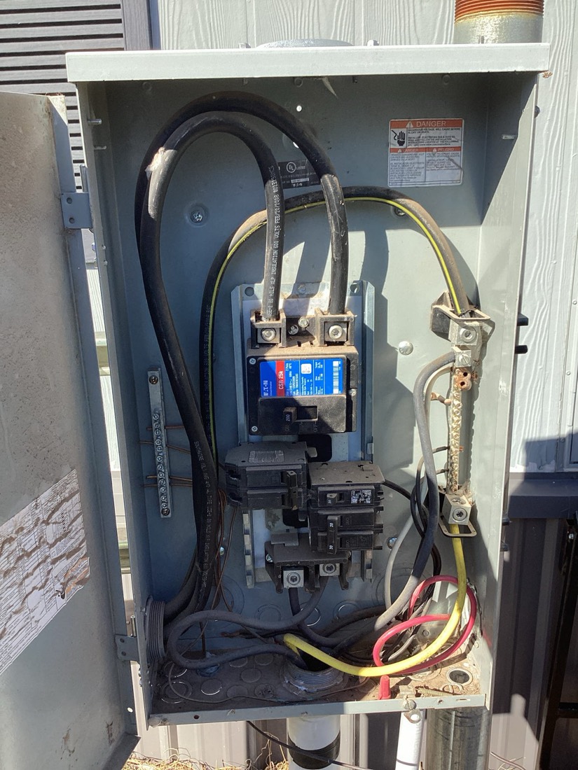 Installed electrical service panel with black cables and brass connections