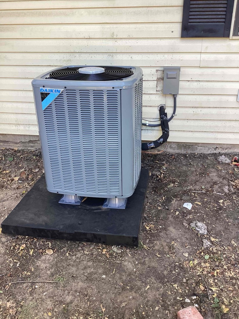 Daikin AC condenser on concrete pad against house