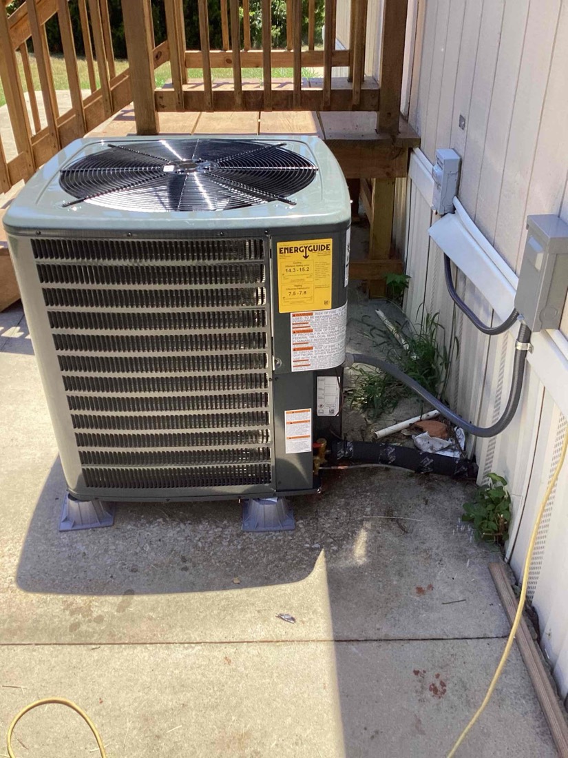 Outdoor AC condenser unit mounted on leveling pad with refrigerant lines connected
