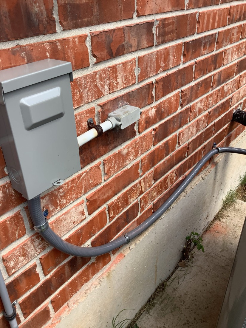 Outdoor AC unit mounted on brick wall with white conduit and copper lines