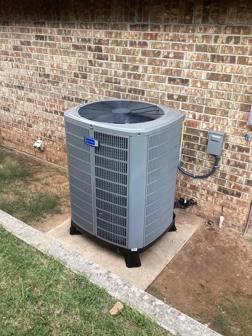 New AC unit installed on concrete pad against brick wall.