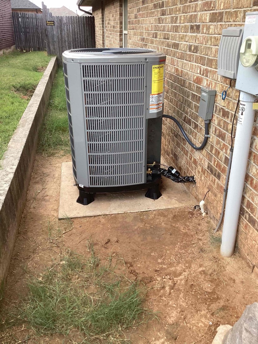 Newly installed AC condenser unit on concrete pad next to brick home.