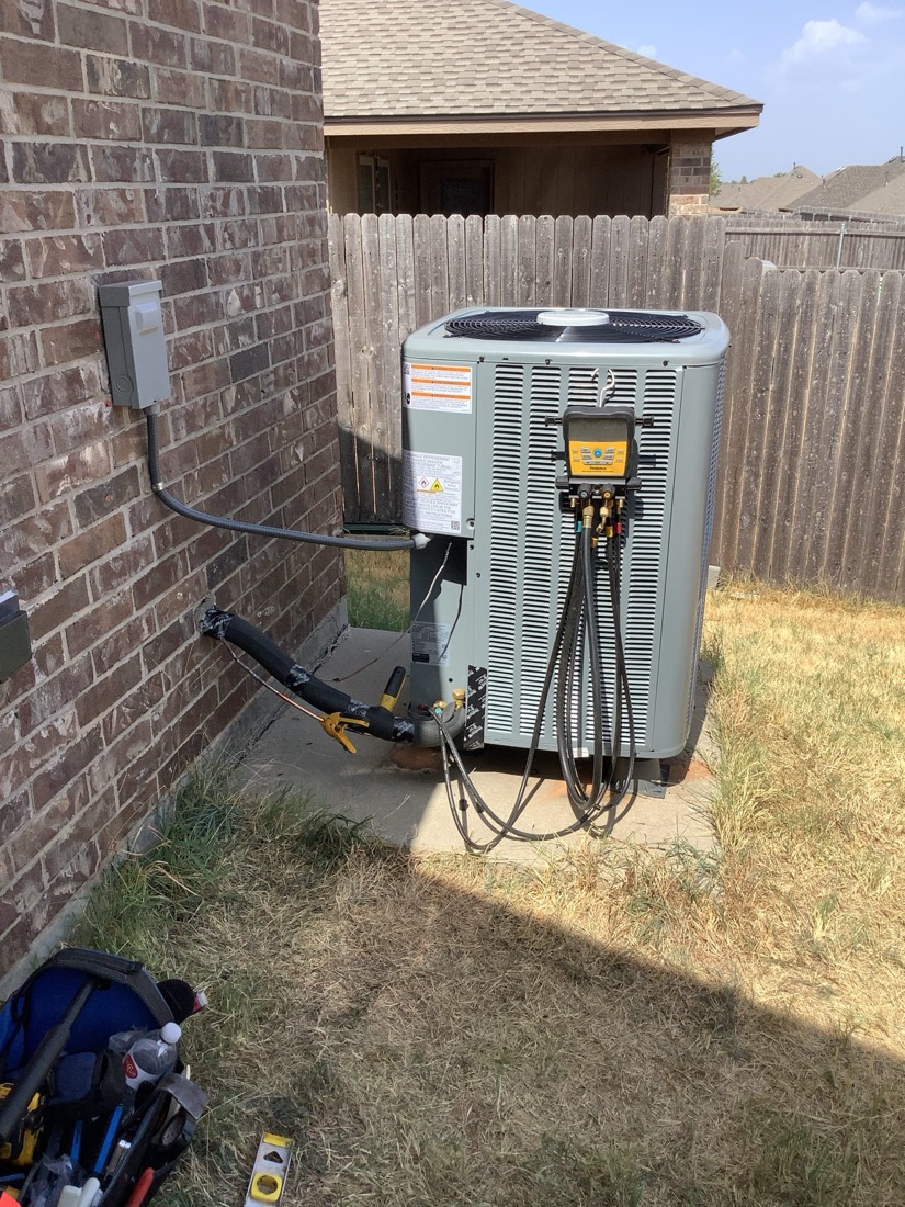 Installed air conditioning condenser unit with refrigerant lines and disconnect switch on brick wall.