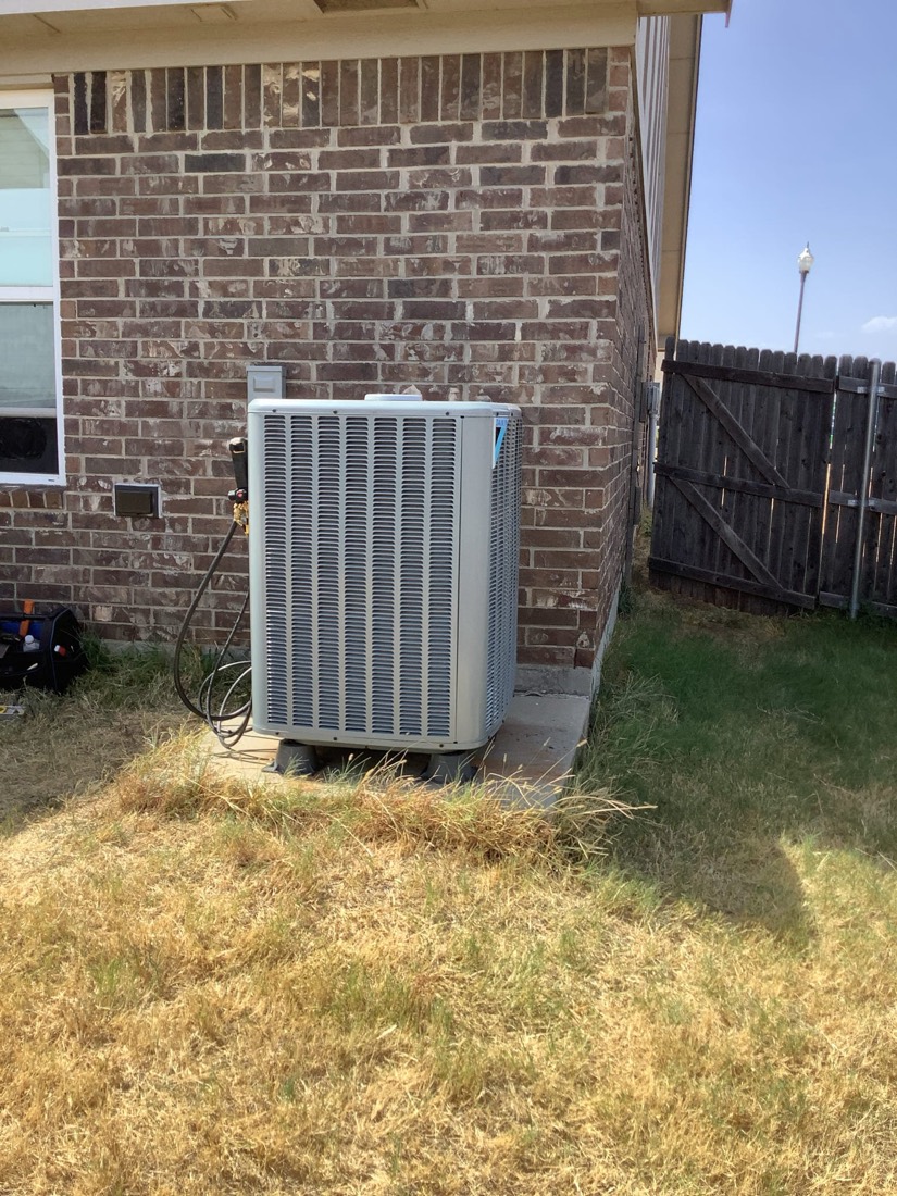 Newly installed exterior air conditioning condenser unit against brick wall.