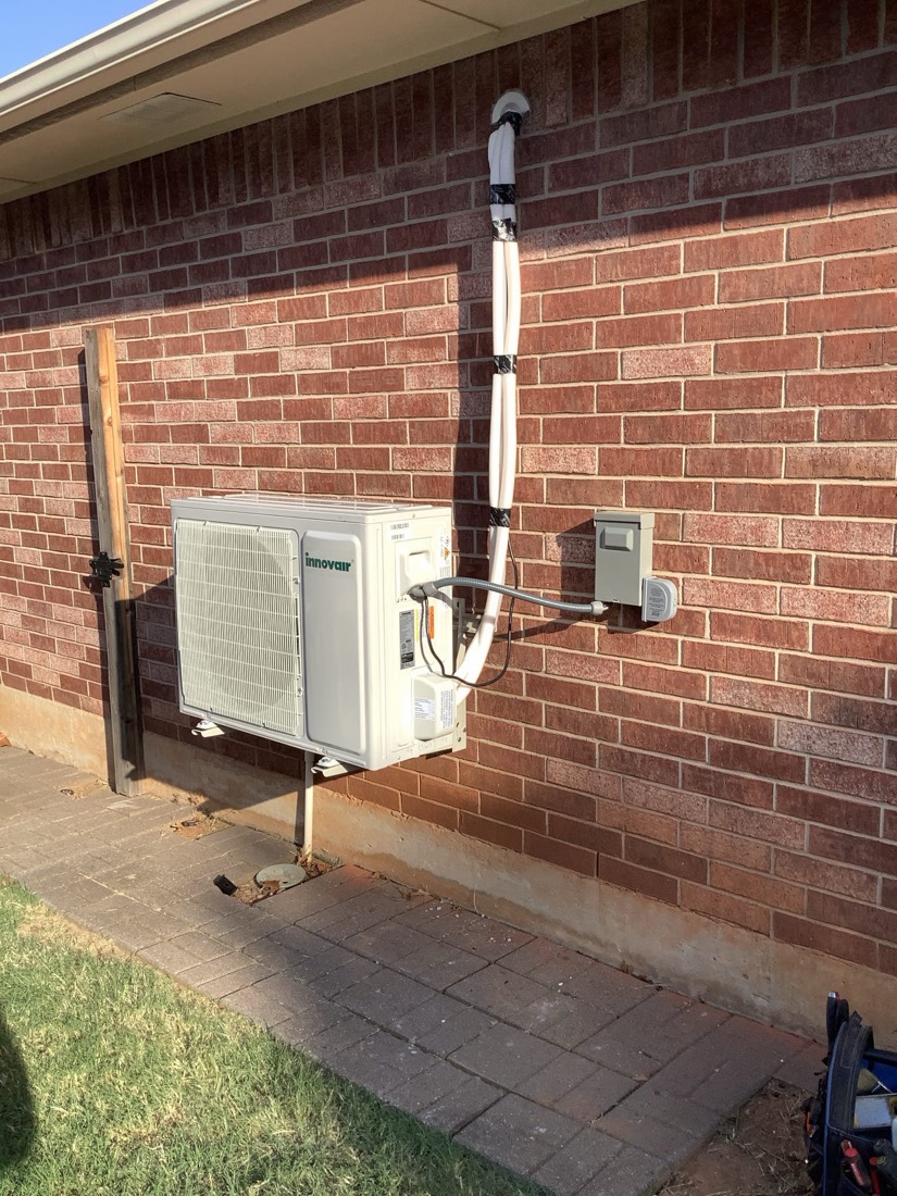 Outdoor mini-split HVAC condenser unit installed on brick house exterior.