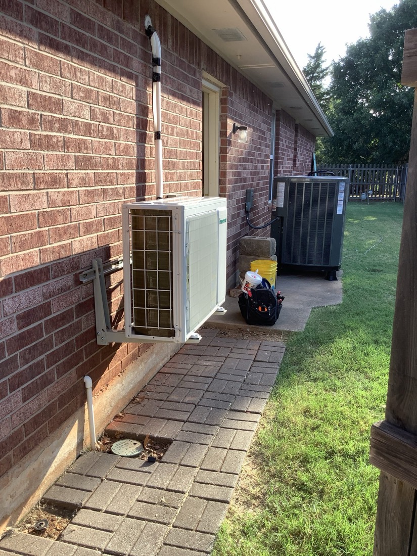 Newly installed AC condenser unit mounted outside brick residence.