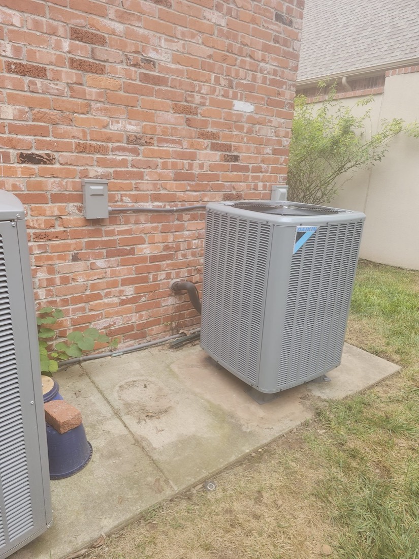 Clean installed AC unit on concrete foundation with brick wall backdrop.