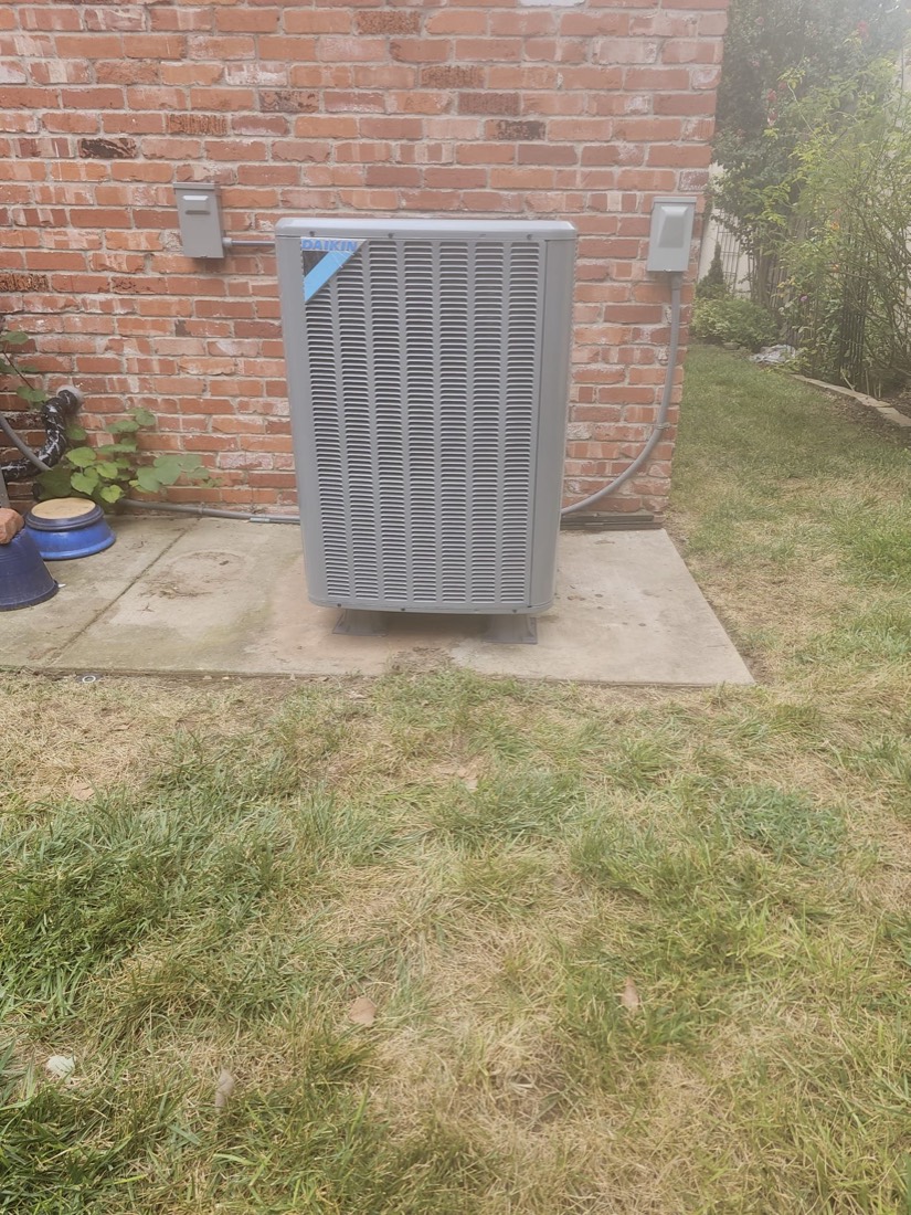 Gray Daikin air conditioning unit installed on concrete pad against brick wall.