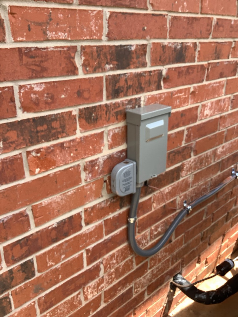 Gray outdoor electrical disconnect switch mounted on red brick wall.