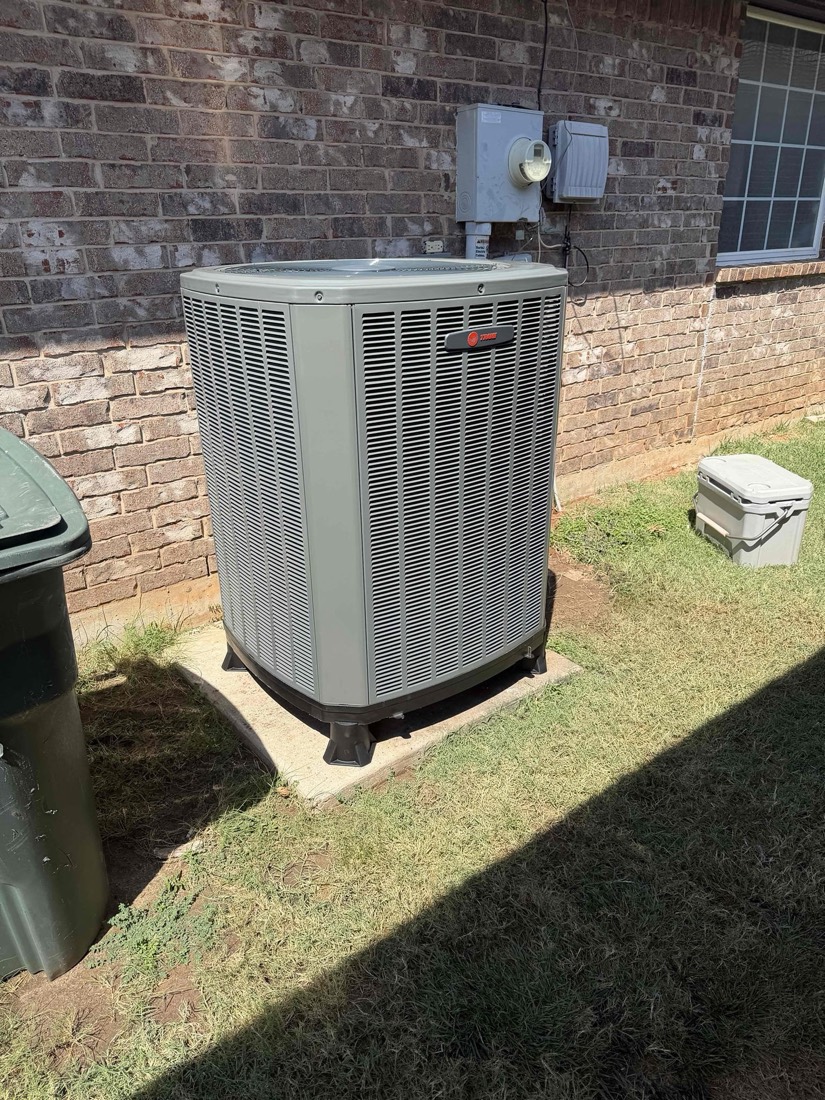 Newly installed AC condenser unit against brick exterior wall
