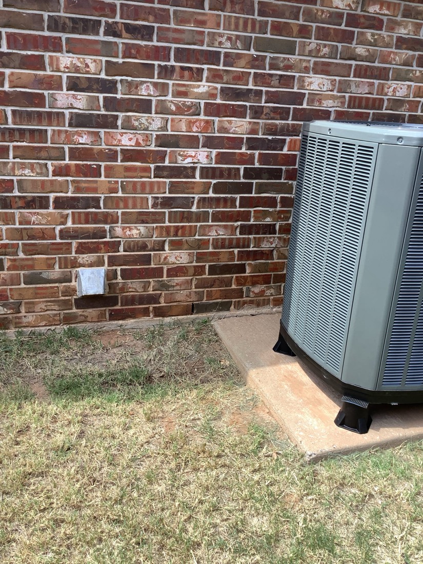 Outdoor HVAC condenser unit on concrete pad against brick wall.