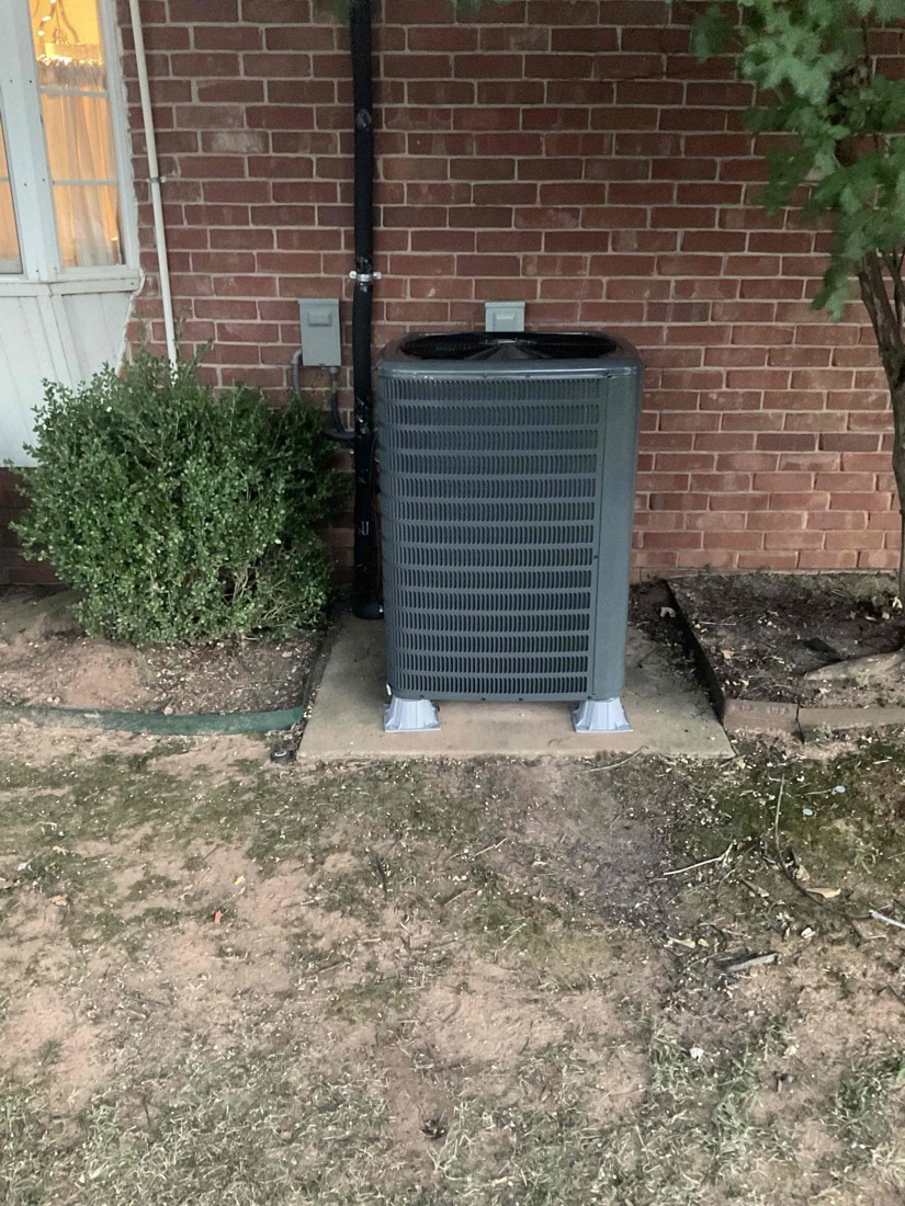 Air conditioning unit mounted on white pads in front of brick house