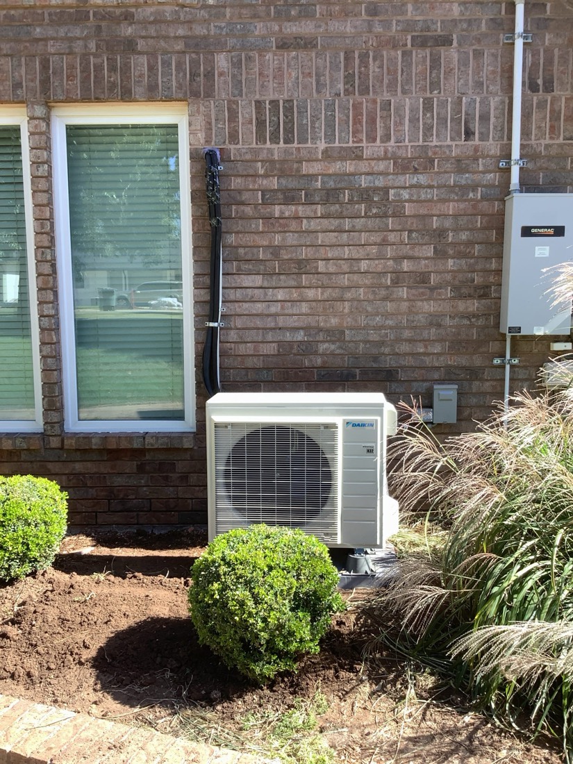 Outdoor AC/heat pump condenser unit neatly installed with landscaping.