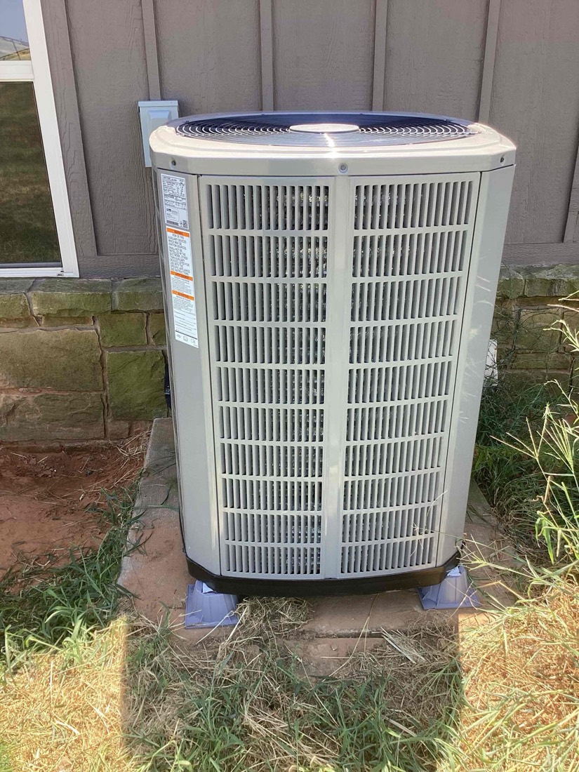Outdoor AC condenser freshly installed on concrete pad next to home foundation.