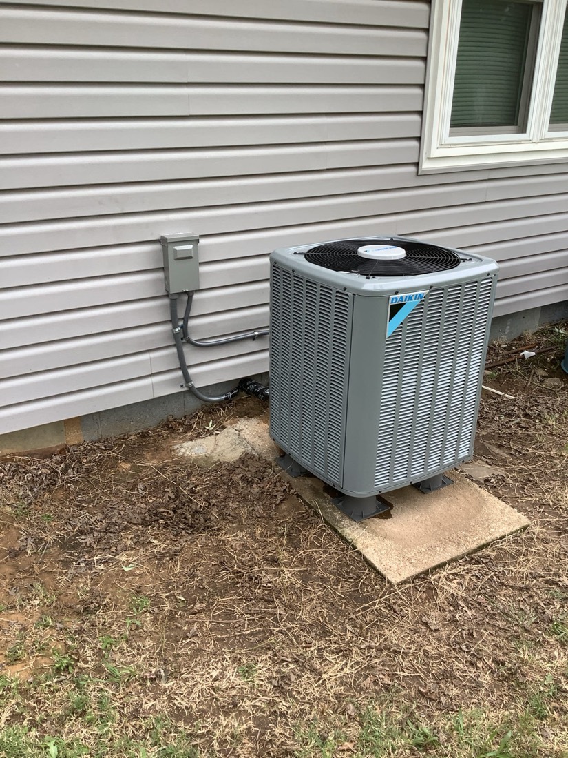 New HVAC condenser with blue label on concrete pad against vinyl siding