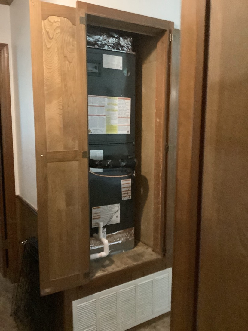 Installed air handler unit mounted in wooden cabinet with ductwork.