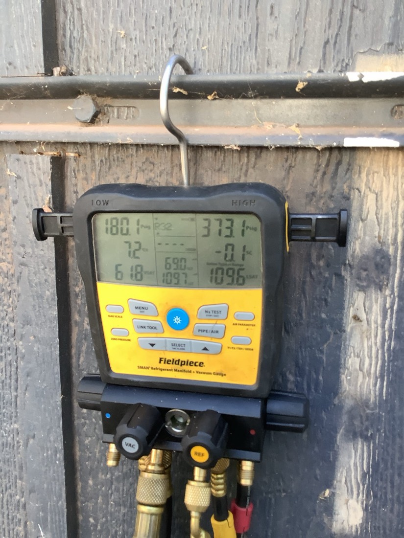 Yellow Fieldpiece diagnostic meter connected to brass manifold block on copper refrigerant lines.