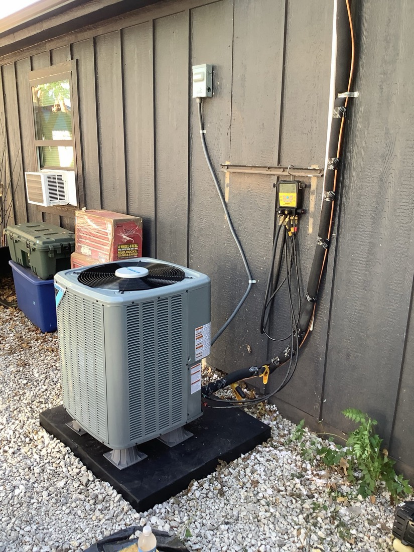 Installed AC condenser unit with copper refrigerant piping and disconnect on equipment pad.