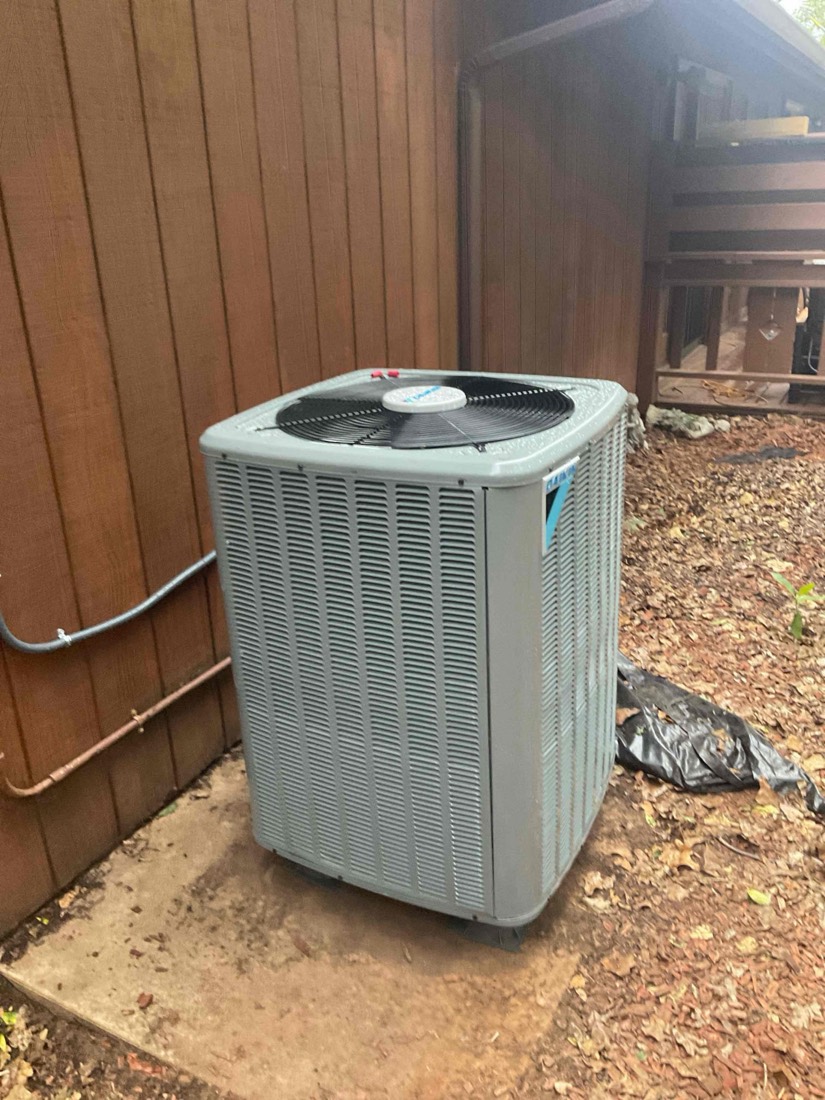 White AC condenser unit on concrete foundation with copper and blue refrigerant lines visible.