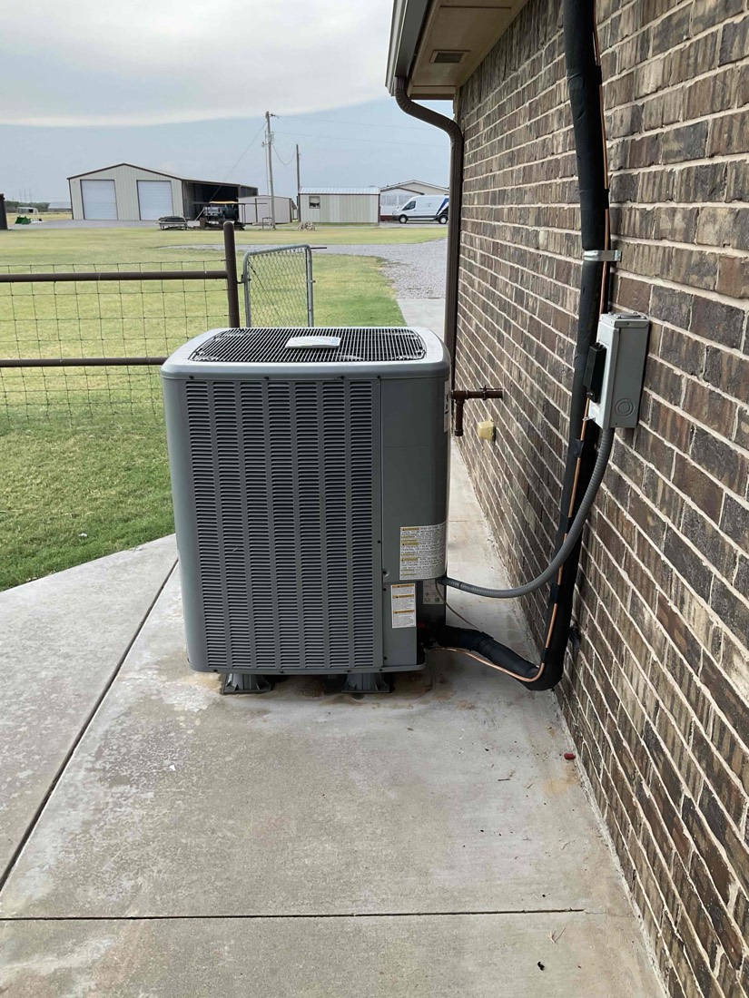 New air conditioning unit installed on concrete pad next to brick home