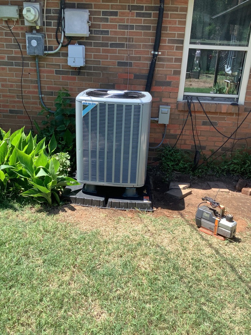 Daikin AC condenser unit on concrete pad against brick wall