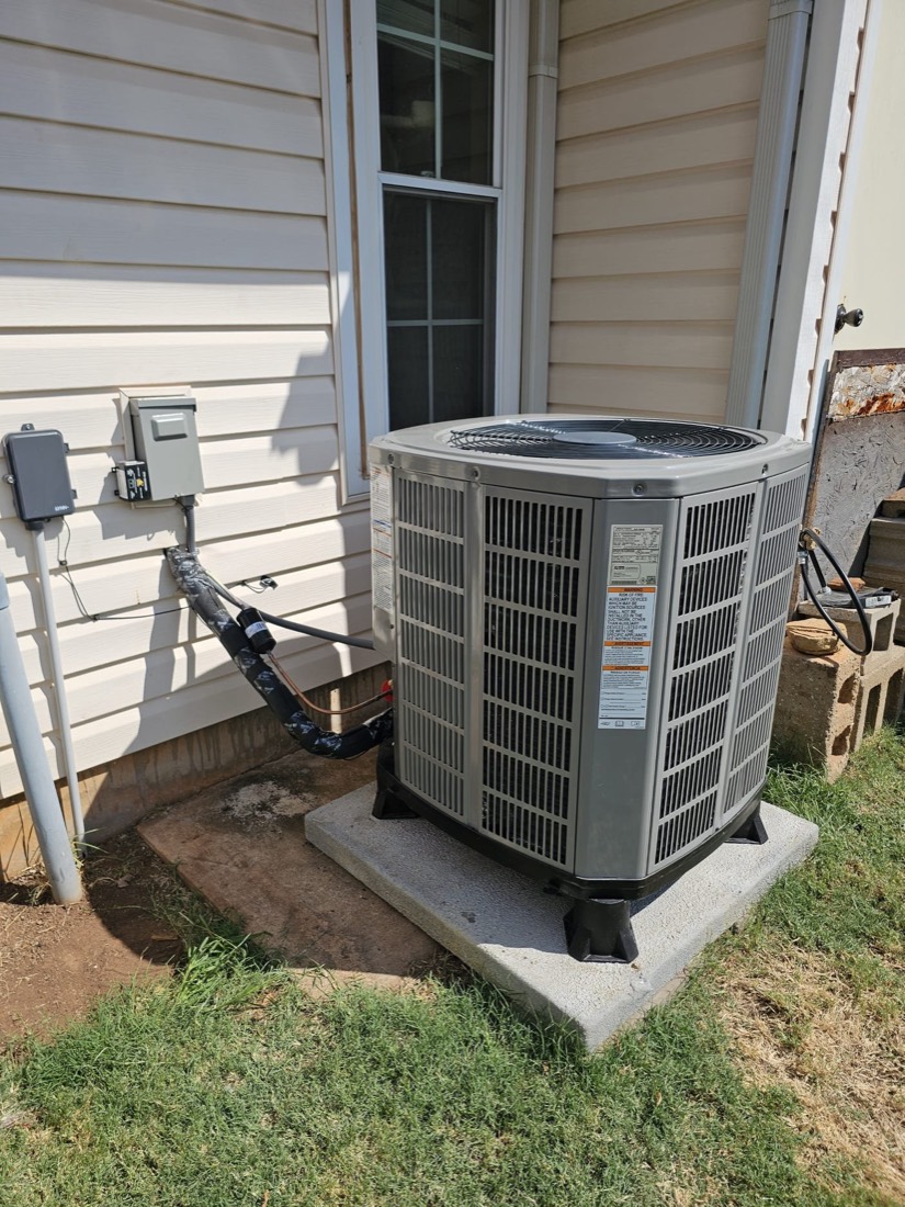 New air conditioning condenser unit on concrete pad outside residential home