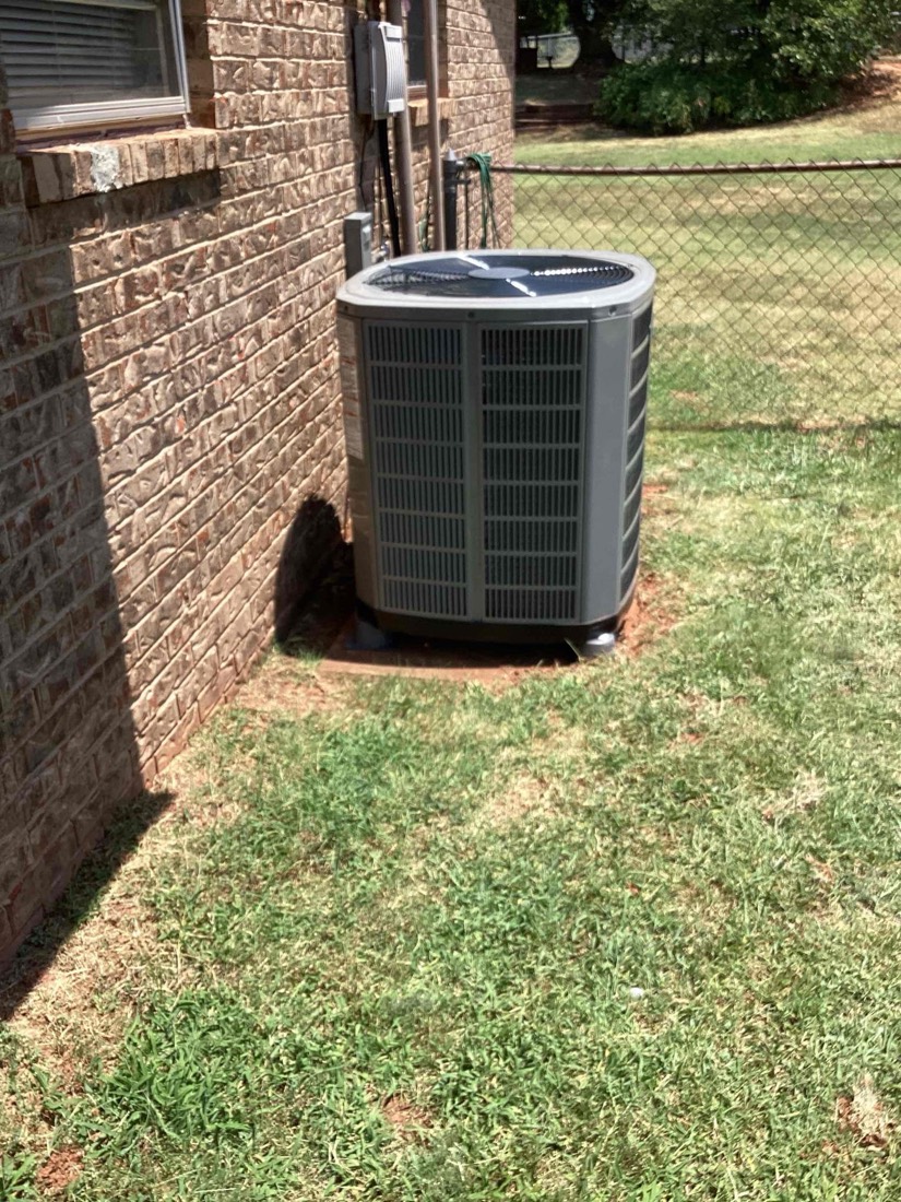 Outdoor AC condenser unit installed next to brick foundation
