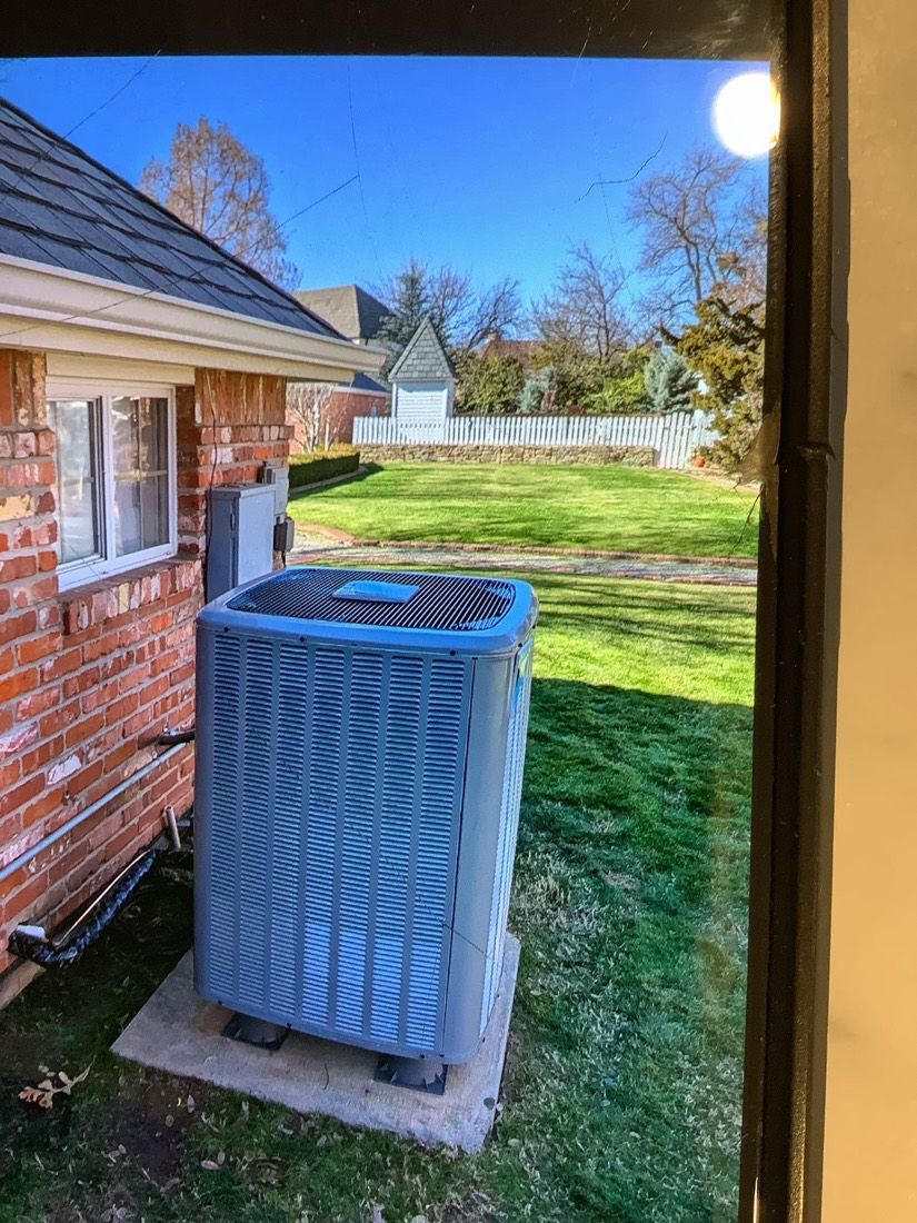 New AC condenser unit on concrete pad next to brick home exterior.