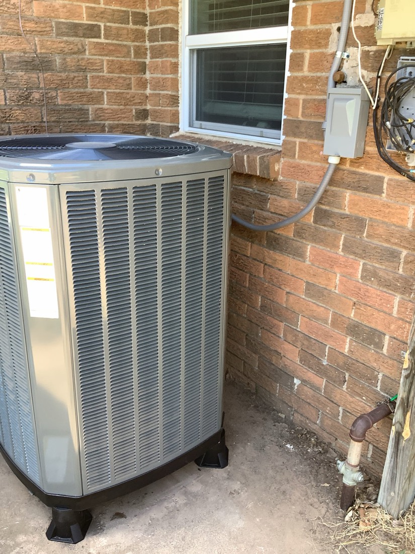 New AC condenser unit installed against brick exterior wall