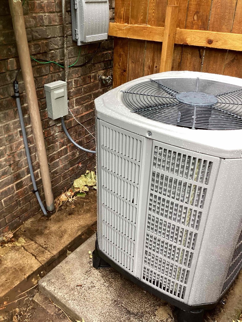 New AC condenser with disconnect switch mounted on brick exterior.