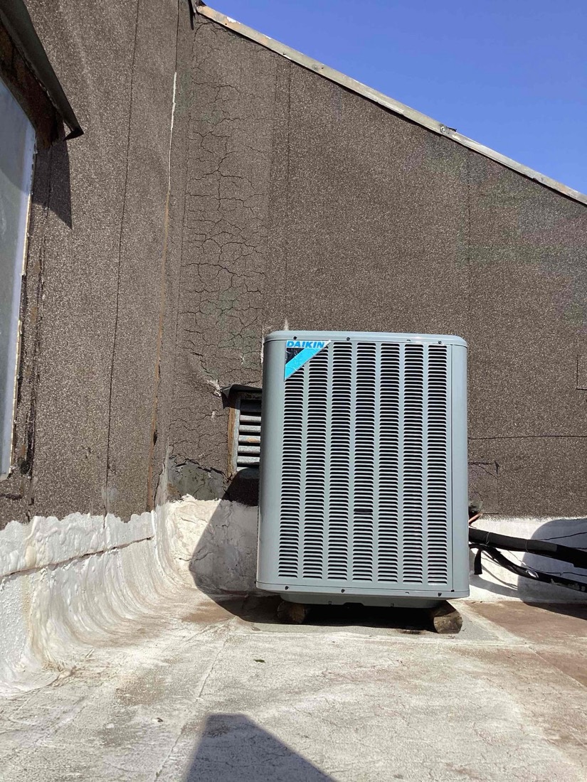 White HVAC condenser unit installed on concrete pad against exterior wall