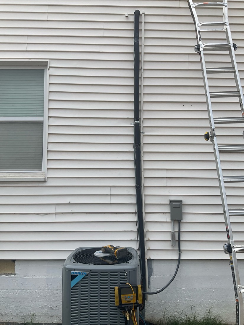 AC unit with insulated refrigerant line running up house.