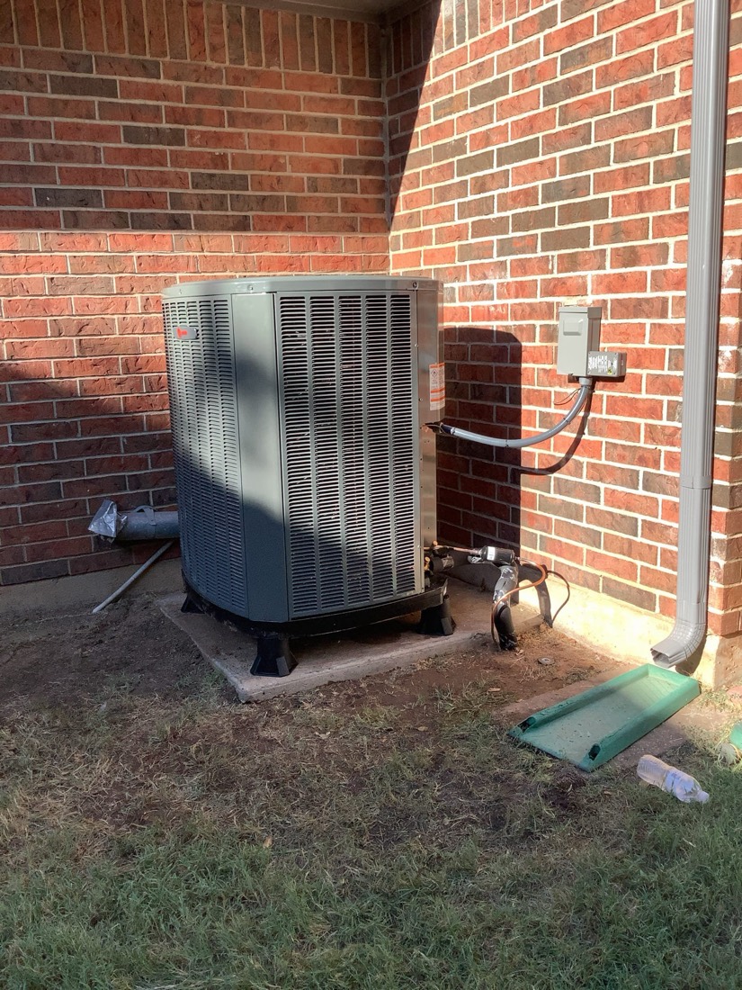 Newly installed AC condenser unit against brick wall with connecting lines.