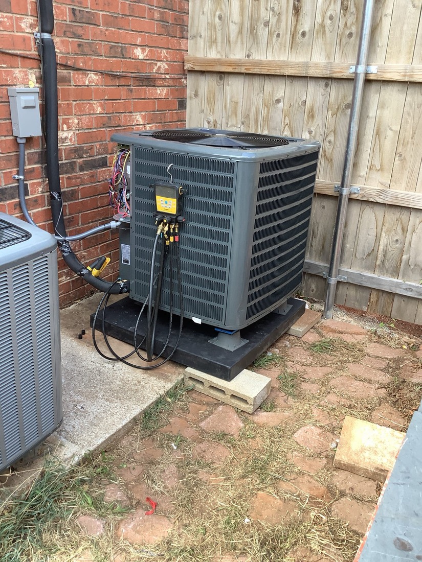 Newly installed AC condenser unit mounted on pad with piping and electrical connections